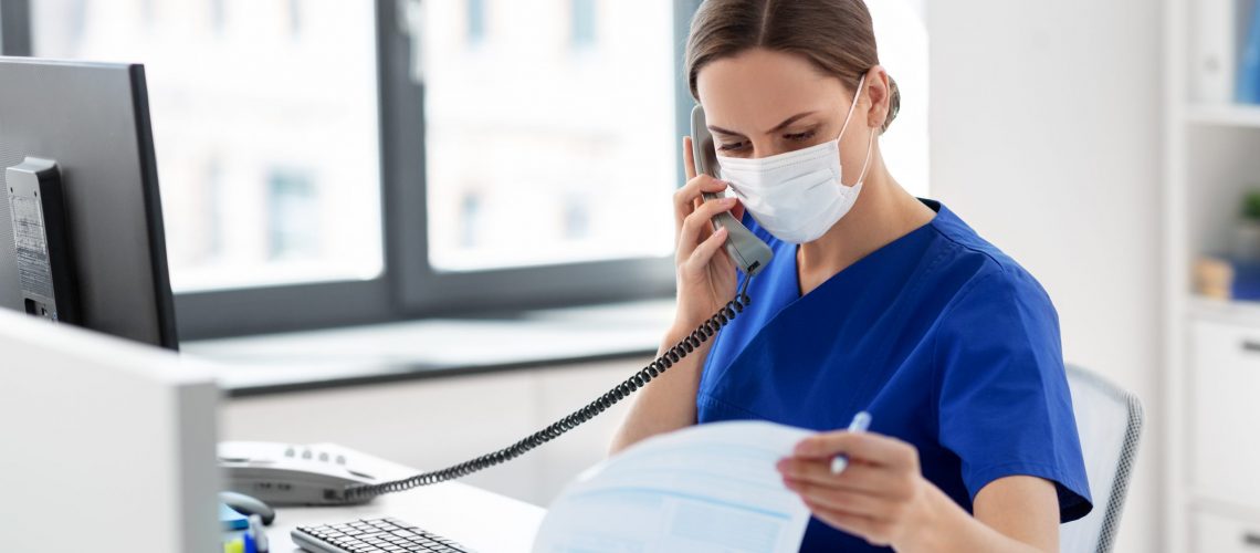 medicine, people and healthcare concept - female doctor or nurse wearing face protective medical mask for protection from virus disease with computer and clipboard calling on phone at hospital