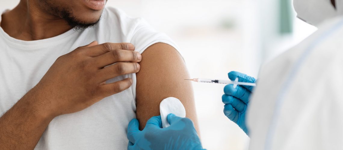 Vaccination and immunization concept. Cropped of young black man receiving vaccine shot during coronavirus pandemic. Closeup of doctor in PPE making injection in shoulder for male patient