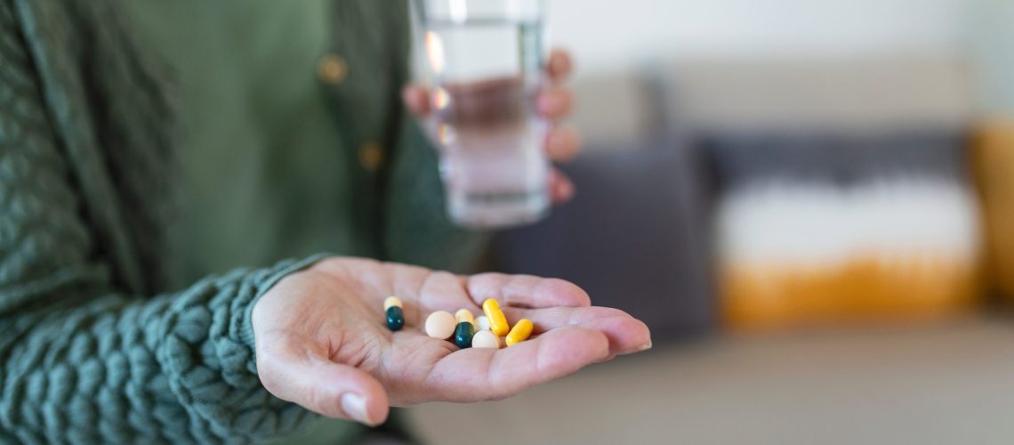 Senior woman takes pill with glass of water in hand.